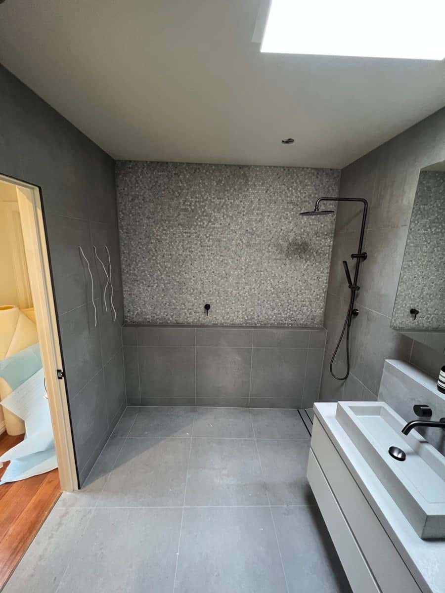 Soft grey bathroom with large-format tiles and a mosaic feature wall inside the shower zone.