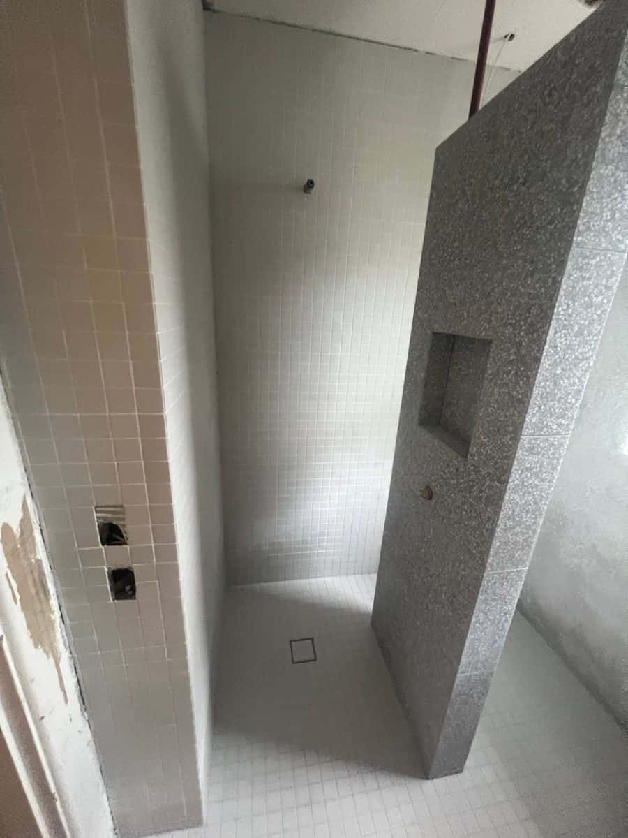 Shower with white floor mosaics and a terrazzo partition wall with a built-in niche.