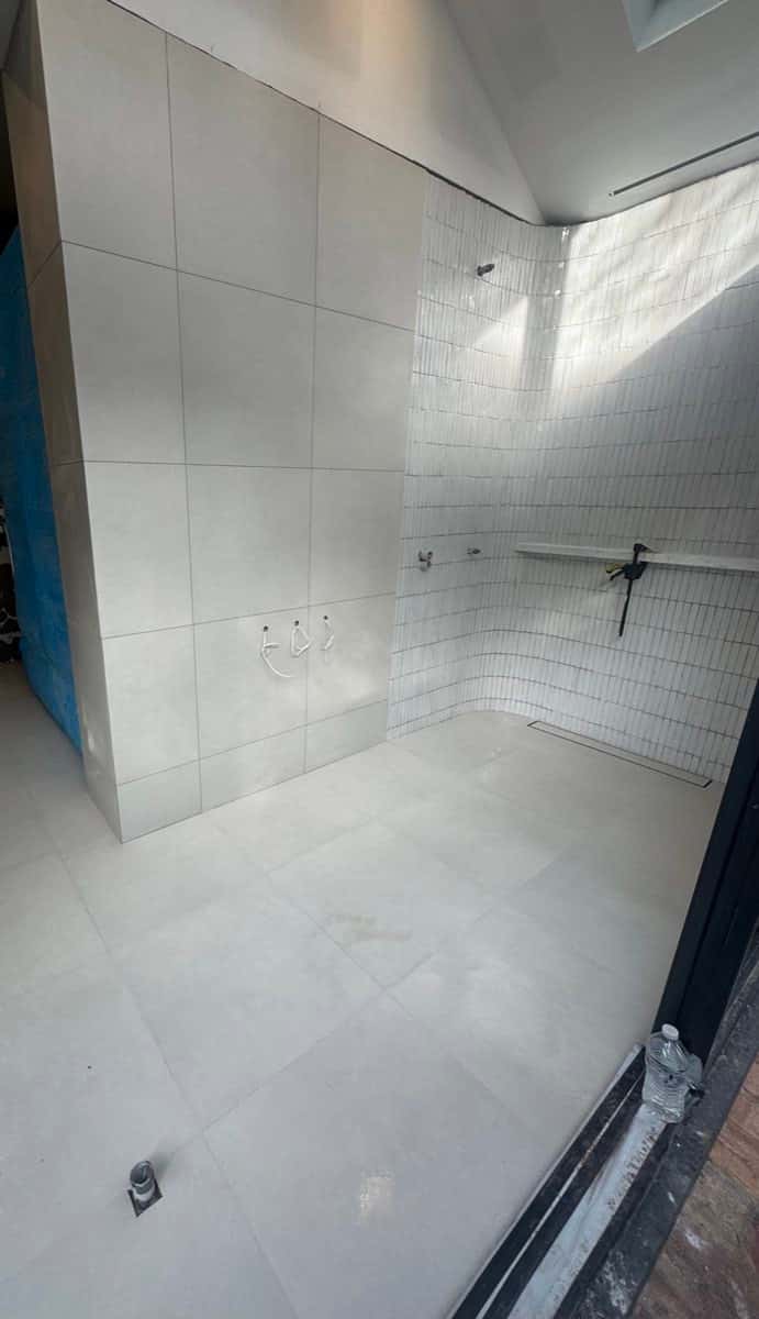 Bathroom with large-format light floor tiles and narrow vertical wall tiles in the shower zone.